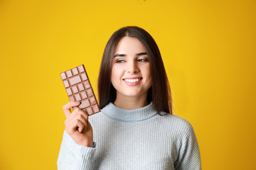 Beautiful young woman with tasty chocolate on color background