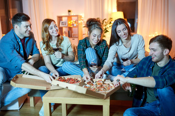 Wall Mural - friendship, food and leisure concept - happy friends eating pizza and drinking non-alcoholic red wine at home in evening