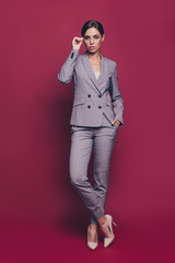 Wall Mural - Vertical full length body size view portrait of nice classy pretty attractive professional lady ceo boss chief in gray checkered suit high heels isolated over maroon burgundy marsala pastel background