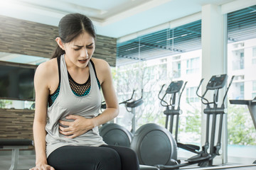 Wall Mural - Young asian woman having pain in stomach. Asian sportswear stressful woman having stomachache during her period.