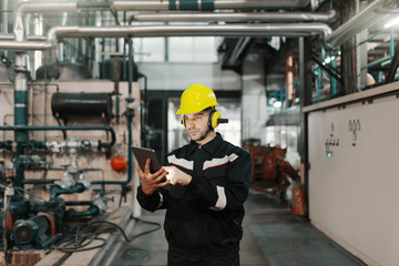 Wall Mural - Caucasian worker in heavy industry plant with helmet and in uniform using tablet for work.