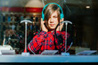 © Iryna - Stylish casual hipster teenager boy at plaid red shirt, backpack using new headphones at electronics store. Photo taken through the window