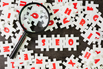 Wall Mural - Search Engine Optimization, SEO concept, white puzzle jigsaw with alphabet building the word SEO at the center of dark chalkboard with magnifier glass.