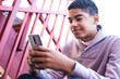 © Oleksandr - A black man uses a mobile phone. Teen sitting on the stairs playing a game on the smartphone. Afro american boy is writing a message.