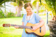 © simona - Cheerful and happy old aged senior caucasian woman smiling and having fun playing a  guitar and dong music in outdoor park leisure activity - retired happy people with interests enjoying new life
