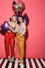 Poster - Image of two european girls 20s in stylish outfit laughing and holding festive balloons