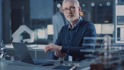 Poster - Professional Electronics Design Engineer Wearing Glasses Works on Laptop Computer in Research Laboratory. In the Background Motherboards, Circuit Board, Heavy Industry Robotic Components