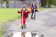 © Irina Schmidt - Two little kids boys riding on push scooters on the way to or from school. Schoolboys of 7 years driving through rain puddle. Funny siblings and best friends playing together. Children after school