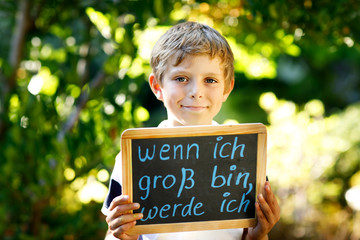 Happy little kid boy with chalk desk in hands. Healthy adorable child outdoors On desk When I grow up I want to be in German with dream profession