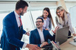 © Mediteraneo - Group of young business people working and using laptop while sitting at the office desk together. Selective focus.