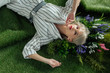 © LIGHTFIELD STUDIOS - high angle view of beautiful stylish young woman looking at camera while lying on artificial grass with fern and flowers