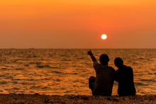Silhouetted Couple Sitting, And Relax On Beach In Love And Embrace, Sunset In The Beach. Family And Lifestyle Concept