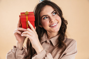 Sticker - Excited young pretty woman posing isolated over beige background wall holding present gift box.