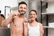 shirtless boyfriend and attractive girlfriend brushing teeth in bathroom