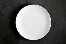 Empty White Plate On Black Background Table. Flat Lay, Top View, Copy Space