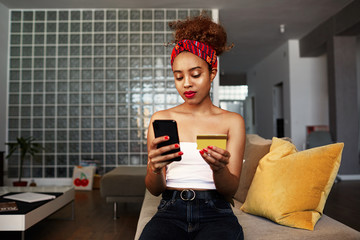 Young attractive black african female holding hands credit card and mobile phone hands. Technology, internet banking, e-commerce and online shopping