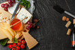 © MONIUK ANDRII - Mix cheese on dark background on wood board with grapes, honey, nuts, tomatoes and basil. Top view.