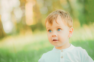 portrait child male wearing a stylish white shirt and dark green pants  with a sweet smile. Nature green background