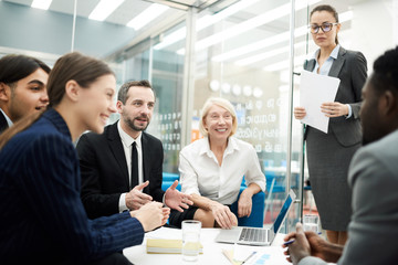 Group of cheerful business people brainstorming ideas for startup project sitting at coffee table in office, copy space