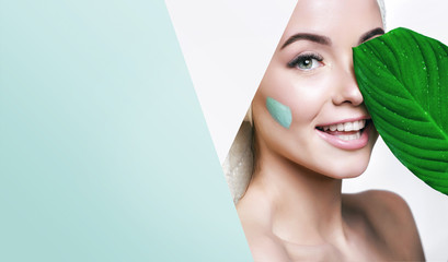 portrait of beautiful woman with healthy glow perfect smooth skin holds tropical leaf, look into the