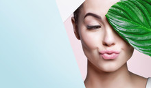 Portrait Of Young Beautiful Woman With Healthy Glow Perfect Smooth Skin Holds Green Tropical Leaf, Look Into The Hole Of Colored Paper. Model With Natural Nude Make Up. Fashion, Beauty, Skincare.