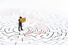 Miniature People, Businessman In The Labyrinth Or Maze Figuring Out The Way Out. Business Concept, Finding Solution, Strategic, And Business Opportunity.