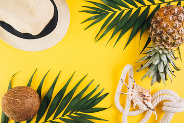 Wall Mural - Summer flat lay background. Palm leaves, coconut, pineapple, sunglasses, rope, straw hat and shell on yellow background.