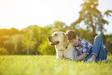 Young Cheerful Boy Resting At The Park With His Dog
