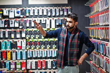 indian man customer buyer at mobile phone store choose a case for his smartphone. south asian people