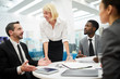 © Seventyfour - Multi-ethnic group of people sitting at table during meeting in office, focus on mature businesswoman talking to colleagues