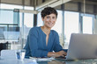 © Westend61 - Portrait of confident businesswoman sitting at desk in office with laptop