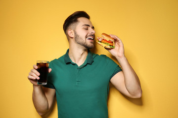 Wall Mural - Handsome man with tasty burger and cola on color background