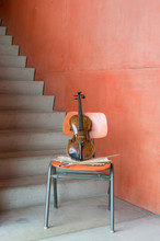 Violin, Bow And Sheet Music On Wooden Chair At Staircase