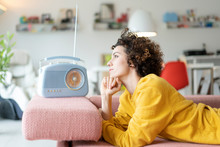 Woman Lying On Couch Listening To Music With Portable Radio At Home