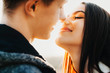 © Strelciuc - Side view close up portrait of charming european couple trying to kiss with closed eyes smiling against sunset while dating outside against sunset.