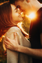 Close Up Side View Portrait Of A Attractive Caucasian Couple Embracing And Laughing Before Kissing Against Amazing Sunset Light.