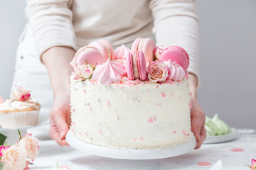 Confectioner puts a beautiful white cake with macarons and roses on a table