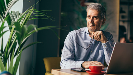 thoughtful man using laptop in cafeteria