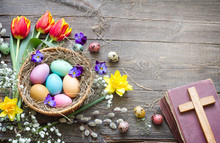 Easter Colorful Eggs In The Nest With Flowers On Vintage Wooden Boards With Bible And Cross
