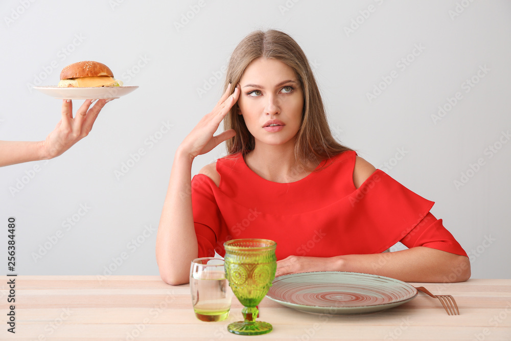 Hand suggesting tasty burger to woman sitting at table