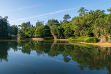 Fototapeta Krajobraz - Trees and sky reflecting in a small lake in public gardens in Singapore