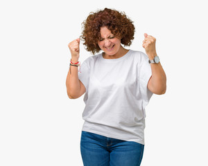 Beautiful middle ager senior woman wearing white t-shirt over isolated background very happy and excited doing winner gesture with arms raised, smiling and screaming for success. Celebration concept.