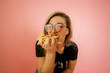 young beautiful blonde girl model with appetite eating fast food, French fries holding in hand, on a pink background