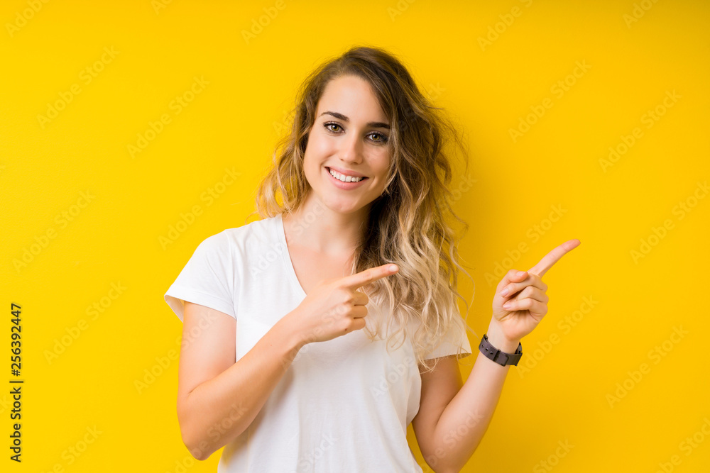 Young beautiful blonde woman over yellow background smiling and looking at the camera pointing with two hands and fingers to the side. - obrazy, fototapety, plakaty 