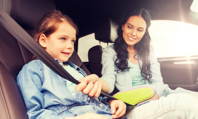 Wall Mural - family, transport, road trip and people concept - happy woman fastening child with safety seat belt in car