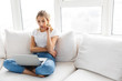 Image of puzzled woman using silver laptop while sitting on sofa in living room