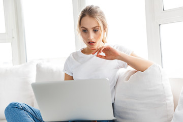 Poster - Image of caucasian woman using silver laptop while sitting on sofa in living room