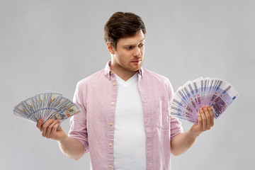 Wall Mural - money, finance, business and exchange rate concept - uncertain young man with hundreds of euro and dollar bank notes over grey background