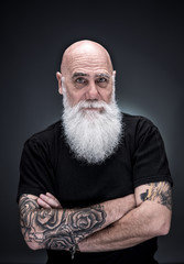 studio portrait of a bald man with tattooed arms and white beard