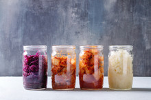 Variety Of Fermented Food Korean Traditional Kimchi Cabbage And Radish Salad, White And Red Sauerkraut In Glass Jars In Row Over Grey Blue Table.